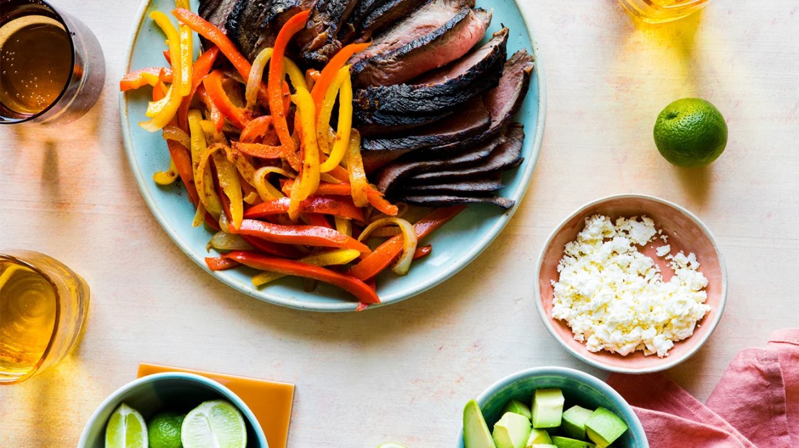 The prepared ingredients for steak fajitas — including meat, veggies, and cheese — on a table.
